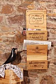 Newspaper rack hand-crafted from old wine crates hanging on rustic stone wall next to black bird figurine
