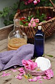 An arrangement of home-made rosewater in a blue bottle next to a towel, roses and rose petals
