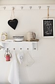 Heart-shaped board hanging from wall hook and shelf holding classic alarm clock, ceramics and reel of red and white ribbon; sketch of rabbit on chalk board