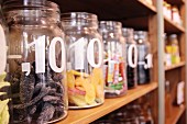Assorted sweets in open storage jars, labelled with price per item, on wooden shelving