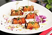 Rolled aubergine slices filled with cheese, decorated with bamboo skewers, dried flowers and slices of red onion