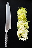 Sliced white cabbage with a Japanese kitchen knife on a black background