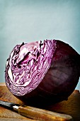 A large wedge of red cabbage on a wooden board with a knife
