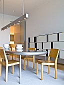 Wooden chairs around table with curved top below designer pendant strip light; contemporary shelving with white, sliding fronts against wall