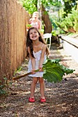 Kleines Mädchen hält ein grosses Rhabarberblatt im Garten