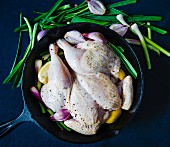 Herb chicken with shallots and lemon on a bed of spring onions, ready to cook, in a black pan