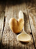 A heart-shaped potato and a wooden spoon on a wooden surface