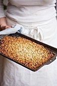 A woman holding a baking sheet of toasted pine nuts