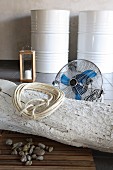 Coiled rope on whitewashed tree trunk on floor in front of fan with white-painted metal drums in background