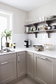 Kitchen base units with modern panelled fronts and open shelving in shades of grey, white work surfaces and wall tiles