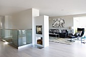 Large interior with dark sofa set and double-sided fireplace in partition; head of staircase with glass balustrade in foreground