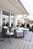 Grey sofa set, side tables and rug on balcony adjoining glass facade of Scandinavian wooden house