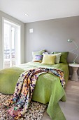 Classic lamp on side table next to bed with lime green throw and blanket with graphic pattern