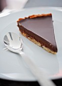 A slice of chocolate tart on a plate with a spoon