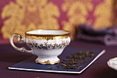 A teacup with a gold edge and leaves of green tea