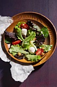 Mixed salad with mozzarella, tomatoes and walnut pieces in a wooden bowl