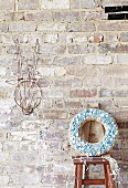 Jute wreath with pastel blue buttons stuck in front of a rustic brick wall, next to it stylized animal trophy decorated with fairy lights