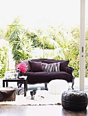 Sofa mit violettem Bezug, Poufs und Sitzkissen; Getränke auf schwarzem Couchtisch und auf weißem, flokatiartigem Teppich
