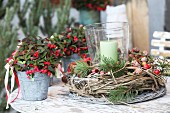 Plants with red berries in small metal buckets and candle lantern in willow wreath