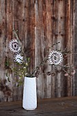 weiße Häkelsterne auf Zweige gehängt in weisser Porzellanvase vor rustikaler Holzwand; Vintage-Weihnachtsflair