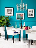 Replica designer lamp above small dining set; framed art prints on turquoise wall
