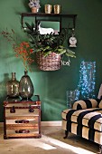 Striped armchair, fairy lights in glass vessels, demijohns on side table and basket of Christmas decorations on green wall