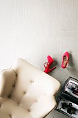 White, leather armchair, red ladies' shoes & magazine rack on white tiled floor with mixture of surface structures