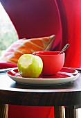 Apple with bite missing next to bowl on red plate on side table