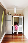 Kleines Mädchen an Geschirrschrank neben Kühlschrankkombination