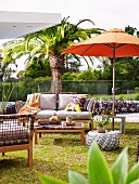 Terrace space in front of palm tree and glass balustrade, orange parasol, sofa and wicker furniture with retro flair