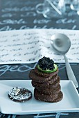 A stack of pumpernickel topped with a slice of cucumber and caviar next to a model skier