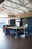 Küchentheke mit Barhockern auf Holzboden in hohem offenem Wohnraum mit weiss lackiertem Dachstuhl