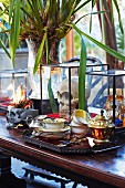 Palm-tree-type plants amongst antique tea service on tray and skull in glass case on Colonial-style wooden table