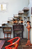 Vintage Armlehnstuhl mit rotlackiertem Gestell und Büste auf Stele neben Treppenaufgang mit frei auskragenden Steinstufen, darunter Schränkchen im Kolonialstil