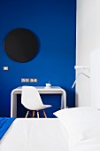 Color design in the bedroom with designer writing desk and classic chair in front of a royal blue wall with a black disc
