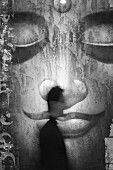 Large size, black and white projection of the face of a Buddha; in front a blurry image of a man in profile