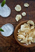 Two glasses of gin and tonic with ice cubes, and a wooden bowl of crisps