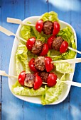 Meatball skewers with tomatoes on lettuce leaves
