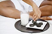 Low section of woman sitting on bed with milk and cookies