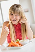 A woman eating raw vegetables with dip