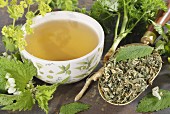 A cup of herbal tea with ingredients (lady's mantle, lemon balm, parsley root, dead-nettle)