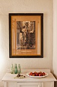 Fruit dish on white cabinet, old framed photo on wall in corner of room