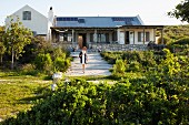 Woman walking down gravel path in summery garden; country house with stone base in background