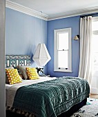 Double bed with quilt, yellow dotted pillows and ethnic pattern on bed head against pastel blue wall