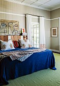 Doppelbett mit blauer Tagesdecke und Kissen vor holzverkleideter Wand und grüner Teppich im Schlafzimmer