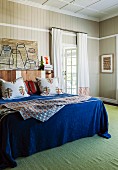 Double bed with blue bedspread and scatter cushions against wood-clad wall and green rug in bedroom