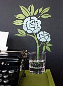 Painted, floral wall decoration and a water glass to an antique typewriter on a console table next