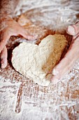 Hands shaping heart-shaped bread