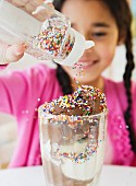 Mädchen schüttet Zuckerperlen über einen grossen Eisbecher