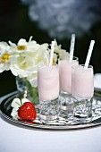 Strawberry milkshakes in small glasses with straws on a silver tray